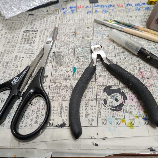 手を抜くのを推奨するのはプラモ制作としてどうなのでしょうか?手を抜くという表現は止めます。自分なりに愛情は注いでいますので・・・。良い例えがありました。料理愛好家の平野レミさんをご存知ですか?私もあの方の料理へのアプローチに準え、ガンプラ愛好家という事にします。モデラーっていうとなんか敷居上がっちゃいますからねwさて続きです。【ランナーからの切り離し】 とりあえずランナー塗装を済ませました。たまに思うのですが、パーツの裏面の色ってドムなら赤だと思いますが、他のMSって大体黒に塗ることが多くないですか?車のボンネットの裏も大体ボディと同じ色じゃないですかね?なので今回は裏面は塗らないです。では、ランナーから切り離しする前には何もしないかというと作業はします。モールドの掘り直しです。使う道具は100均のです。画像の赤い部分はキットに元からあるモールドです。青い方は特にモールドはないですが、掘っておくと墨入れが映えます。赤い方だけでも効果があります。切り離す時はプラモ用の鋏でざっくり切って、精密度の高いニッパーで余分を切るニ段階で対応します。仕上げ用のニッパーは私の持っている工具の方では高めです。ゴッドハンドの片刄ニッパーは壊しそうなので、タミヤのを使っています。3,000円〜4,000円くらいのです。正直高いかと思いますが、ゲート跡を綺麗に処理できるので、作業効率を格段に上げてくれる超便利アイテムなので、ここは頑張って買いましょう。塗装派も無塗装派も同じです。ちなみに私のタミヤニッパーは2代目です。初代は15年以上頑張ってくれました。中のバネが切れました。バネを入れれば復活するかもしれませんが、引退させて道具箱の中で眠っています。【合わせ目消し】ガンプラの大体の宿命として武器の合わせ目ですかね。基本モナカ構造なので、どうしても合わせ目が生じます。特に今回のように長めのライフルは特に合わせ目が発生しやすいです。ここはランナーを見た時から覚悟していました。(合わせ目消しのやり方)1.両面に接着剤(タミヤの白瓶)をドバッと塗り、塗ったあと1〜2分くらい待って「おりゃー」の掛け声と共にくっ付け、接着剤をムニュッとはみ出るまで圧着し、十分に乾燥(1週間なんて言いますね)させてからヤスリで削る。このやり方が一般的ですが、時間がかかるので今回は不採用です。2.合わせ目をそのままにする.変な話、合わせ目上等であれば無視していいかと思います。架空兵器なので、我々がおかしいと思っている合わせ目ですが、実は普通のことなのかもしれないからです。だからどうした!と思えば作業時間は大幅に短縮できます。3.段落ちモールドにする.ここで画像を紹介できませんが、筋彫り堂から出ている段モという工具を使うと段落ちモールド化させて分割線(合わせ目)を有効活用する。4.プラ板とかプラ棒を使って誤魔化す。プラ板を貼ったりして合わせ目を隠しちゃいます。私は最近は3と4の手段を使います。ということで画像はないですが、武器を早めに作っておく事にしました。説明書では武器は比較的最後に作ることが多いですが、最後に合わせ目消しが来ると萎えるので、私は複数を一気に作る時などは先に武器から作ったりします。ちなみにヤスリは水研ぎにしています。削りカスがヤスルと結構出ます。塗装の時よりも気を使ったほうがいいと思います。私はガスマスクみたいなのをつけています。間違って付けたままで宅配便を受け取りに行ったらびびられましたwその3へ続くー。(キャリバーンはバックパック以外は組めています) (2枚目)