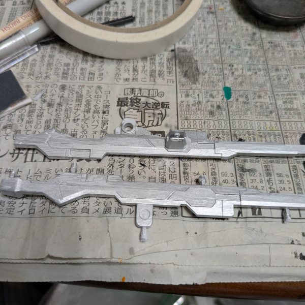 手を抜くのを推奨するのはプラモ制作としてどうなのでしょうか?手を抜くという表現は止めます。自分なりに愛情は注いでいますので・・・。良い例えがありました。料理愛好家の平野レミさんをご存知ですか?私もあの方の料理へのアプローチに準え、ガンプラ愛好家という事にします。モデラーっていうとなんか敷居上がっちゃいますからねwさて続きです。【ランナーからの切り離し】 とりあえずランナー塗装を済ませました。たまに思うのですが、パーツの裏面の色ってドムなら赤だと思いますが、他のMSって大体黒に塗ることが多くないですか?車のボンネットの裏も大体ボディと同じ色じゃないですかね?なので今回は裏面は塗らないです。では、ランナーから切り離しする前には何もしないかというと作業はします。モールドの掘り直しです。使う道具は100均のです。画像の赤い部分はキットに元からあるモールドです。青い方は特にモールドはないですが、掘っておくと墨入れが映えます。赤い方だけでも効果があります。切り離す時はプラモ用の鋏でざっくり切って、精密度の高いニッパーで余分を切るニ段階で対応します。仕上げ用のニッパーは私の持っている工具の方では高めです。ゴッドハンドの片刄ニッパーは壊しそうなので、タミヤのを使っています。3,000円〜4,000円くらいのです。正直高いかと思いますが、ゲート跡を綺麗に処理できるので、作業効率を格段に上げてくれる超便利アイテムなので、ここは頑張って買いましょう。塗装派も無塗装派も同じです。ちなみに私のタミヤニッパーは2代目です。初代は15年以上頑張ってくれました。中のバネが切れました。バネを入れれば復活するかもしれませんが、引退させて道具箱の中で眠っています。【合わせ目消し】ガンプラの大体の宿命として武器の合わせ目ですかね。基本モナカ構造なので、どうしても合わせ目が生じます。特に今回のように長めのライフルは特に合わせ目が発生しやすいです。ここはランナーを見た時から覚悟していました。(合わせ目消しのやり方)1.両面に接着剤(タミヤの白瓶)をドバッと塗り、塗ったあと1〜2分くらい待って「おりゃー」の掛け声と共にくっ付け、接着剤をムニュッとはみ出るまで圧着し、十分に乾燥(1週間なんて言いますね)させてからヤスリで削る。このやり方が一般的ですが、時間がかかるので今回は不採用です。2.合わせ目をそのままにする.変な話、合わせ目上等であれば無視していいかと思います。架空兵器なので、我々がおかしいと思っている合わせ目ですが、実は普通のことなのかもしれないからです。だからどうした!と思えば作業時間は大幅に短縮できます。3.段落ちモールドにする.ここで画像を紹介できませんが、筋彫り堂から出ている段モという工具を使うと段落ちモールド化させて分割線(合わせ目)を有効活用する。4.プラ板とかプラ棒を使って誤魔化す。プラ板を貼ったりして合わせ目を隠しちゃいます。私は最近は3と4の手段を使います。ということで画像はないですが、武器を早めに作っておく事にしました。説明書では武器は比較的最後に作ることが多いですが、最後に合わせ目消しが来ると萎えるので、私は複数を一気に作る時などは先に武器から作ったりします。ちなみにヤスリは水研ぎにしています。削りカスがヤスルと結構出ます。塗装の時よりも気を使ったほうがいいと思います。私はガスマスクみたいなのをつけています。間違って付けたままで宅配便を受け取りに行ったらびびられましたwその3へ続くー。(キャリバーンはバックパック以外は組めています) (5枚目)