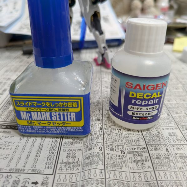 日刊まお大佐5日目です。もう皆様飽きちゃったかなー・・・。今までずっとガンダムルプリスだと思っていましたが、ルブリスなんですね。名前を誤って覚えておりました。ファンの方、失礼しました。さて、5日目ということでキャリバーンもルブリスもカタチになりました。ルブリスの盾とキャリバーンのライフルはもうちょい何とかしたいですが、企画倒れにならないためにも先に進めます。【スミイレ】スミイレといえばエナメル塗料でやるのが一番綺麗に仕上がりますが、いかんせんエナメル塗料はプラを割ります。（ラッカーでもアクリルも割りますが、エナメルは特に）なので、私は関節部にはスミイレしません。組んでからエナメル塗料でスミイレすると割れる可能性が高くなります。負荷に耐えられなくなって折れるようです。この特性を使ったプラの割り方もありますが、ここでは割愛。せっかく組み立てて、写真撮るためにポーズを決めたら、脚が折れたとかもあったので、エナメルのスミイレには及びませんが、私はスミイレ用のガンダムマーカー、油性ペン、シャープペンシル等を使いますが、成人の方のみ推奨ですが、公営ギャンブルの投票用紙とそれに使う鉛筆（選挙でも用意されていますね）が特にオススメです。日頃公営競技で苦渋を舐めている方は、腹いせに投票用紙と鉛筆を少しいただいてしまいましょう。投票用紙は塗料を混ぜたり、ガンダムマーカーの液出しとかに使っています。厚みもあるので便利です。次の作業はデカール貼りになりますが、デカールを貼ったら後はトップコートを吹くだけなので、次回は完成投稿にする予定です。【デカール貼り】私の中では最後の方にやる作業ですが、好きな作業です。ここで道具紹介を。ピンセット以外は必須ではないですが、5つ。⒈ピンセット超重要アイテムです。最初は200円くらいのを使っていましたが、パーツを掴んでいる間にパーツを掴みきれずポロリしてパーツをよく無くすので、ここは清水の舞台から飛び降りました。高いのは医療用だとトンデモない値段がしますが、2,000円から3,000円くらいの模型用精密ピンセットならばきっと期待に応えてくれると思います。大袈裟にいうと刺さりそうなくらい先端が鋭いです。私はスジボリ堂のを使っています。⒉マークセッター貼りたい場所に事前に塗布してデカールを貼ります。これを塗っておくと多少の位置変更ができるので安心です。多少破けても修正できます。⒊デカールトレイプラモ向上委員会から出ている物を使っています。スポンジでぶっちゃけ十分なのですが、これ買ってからデカール貼りが楽しくなりました。ちょっとお高いかな・・・。⒋デカールリペアあまり馴染みがないかもしれませんが、古いデカールの糊を復活させたりするのに使います。絶対復活するわけではないですが、重宝します。ちなみに黄ばんだデカールは日干しで多少直ります。私は真夏に復旧作業します。⒌綿棒水分の拭き取りに使います。100均ので十分かな。100均でも細い綿棒も売っているので、細いのも買っておくと良いかも。【ディティールアップ】描き忘れていました。私がよく使うのはビーズをくっ付ける（バーニアの中とか）やナビゲーションライトを貼る（今回は航行灯はつけてませんが）時に使う接着剤の説明を。セメダイン社から出ているハイグレード模型用セメダインで接着しています。塗った塗料を傷つけにくいので使いやすいです。長々と好き勝手なことを書いてますが、次回でいよいよ最終回になります。土曜日か日曜にはアップしたいですね。お楽しみに。誰もが（きっと）待って（いない）キン○マン〜♪ところで次走走者の方は決まりましたかね？（本来私が声をかけるのでしょうけど・・・）決まらないとバトンを渡さないで次は「大佐と一緒に旧キットを作ろう」が始まってしまいますよ・・・。（3枚目）