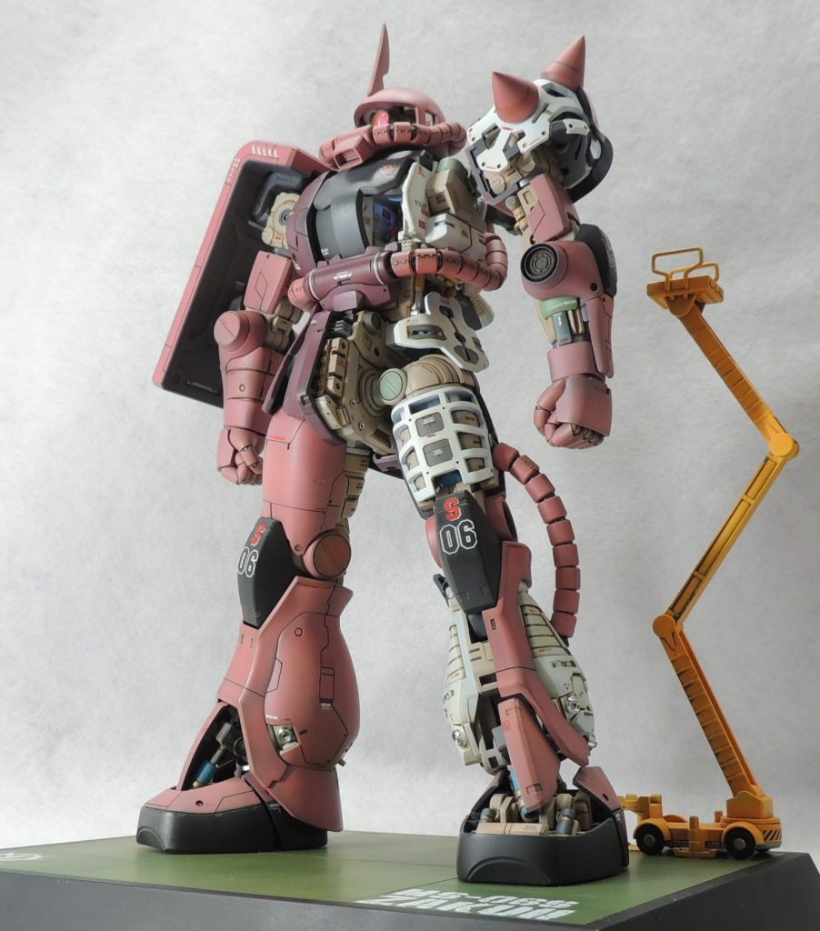 ■台座 キットには台座が付属していないため、タミヤのディスプレイベース・スモール(148mm×108mm)を使用しました。格納庫の一部に見立ててパネルラインのスジ彫りを入れ、下地をブラックサフで塗装した後、油彩によるドッティングにより複雑で奥深い色味を出しています。雰囲気としては、シャア専用ムサイの外壁をイメージしています。 使用したデカールは、ジオン公国章はMG1/100ギャン専用デカールから流用し、文字はスジボリ堂のチッピングデカールを使用しました。