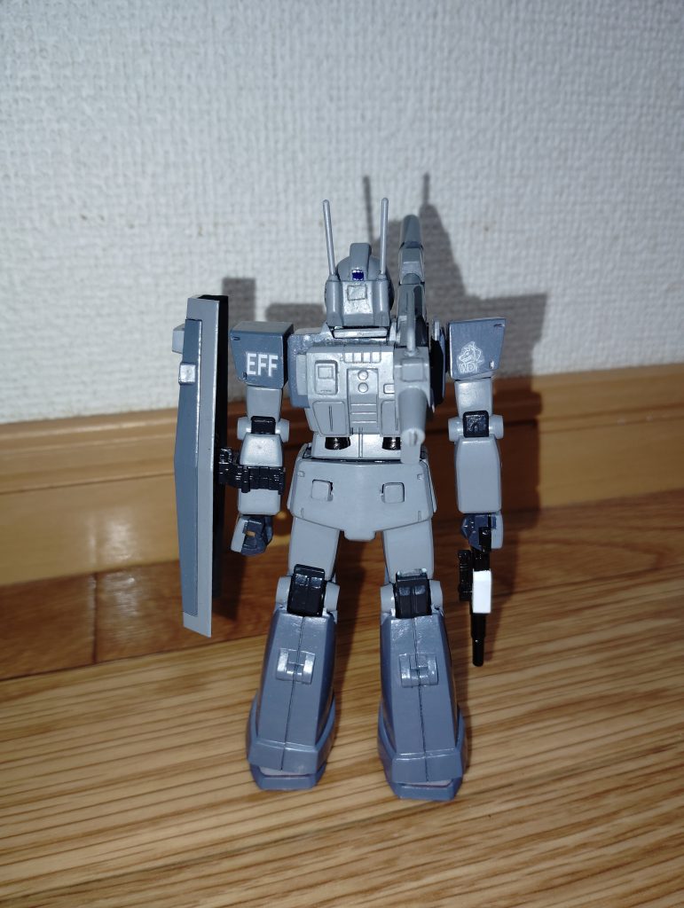 　リアビューです。　バックパックは旧キットMSVのジムキャノンのモノを加工し、バーニア基部をプラ板で追加してから、HGUCジムのバーニアを取り付けてあります。　前回投稿したジム（WD隊）と同様、今回参考にしたのはドリームキャストのゲームソフトである本家「機動戦士ガンダム外伝　コロニーの落ちた地で・・・」ではなく、「戦場の絆」というアーケードゲームです。　そちらのゲームのリプレイ動画（You Tubeで探しました）で確認したところ、ジムキャノンのキットではバックパック左側にあった予備装甲板がオミットされ、代わりにボックス状のディテールが確認できたので、プラ板の箱組みで再現しました。　また、以前投稿したジムキャノンを製作した際「キャノン砲の可動範囲が狭く、仰角が水平より少し高い程度までしか取れない」という致命的な欠点があったので、バックパック右上のキャノン砲後部と干渉する部分をできるだけヤスリで削ってあります。　それから、腰のリアアーマーにはMSVのジムキャノンからキャノン砲の予備弾倉を装備するラッチを移植してあります。　さらに、以前投稿したジムキャノンでは後頭部のアンテナ基部にある四角いディテールをリアカメラとして塗装したのですが（MSVキットの説明書のイラストでも、そのように描写されています）、コチラも「戦場の絆」のリプレイ動画で確認すると、普通のジムなどと同じようなリアカメラになっていたので、アンテナ基部の四角いディテールはあくまで「ただのディテール」として残し、前回投稿したジムと同じように、「ちょんまげ」の後部をリアカメラとしてカッターノコなどで切り出したクリアパーツを塗装したモノを接着剤で取り付けてあります。