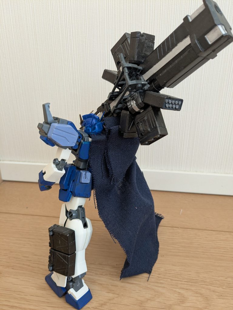 右マントだけのバックショットで１枚。ホントにバズーカ部分がデカすぎるんでしょうね。すごい迫力になってます。前からのショットと十字架砲の持つ向きを変えてあります。こちらのほうだとグリップが見えるので、どこを持って砲撃するのか分かりやすくなってますね。てかこのマントって「火星の砂嵐と磁気から全身を守るために身に着けている」もののはずなので、この状態だと完全に砂と磁気にやられますよね（笑）