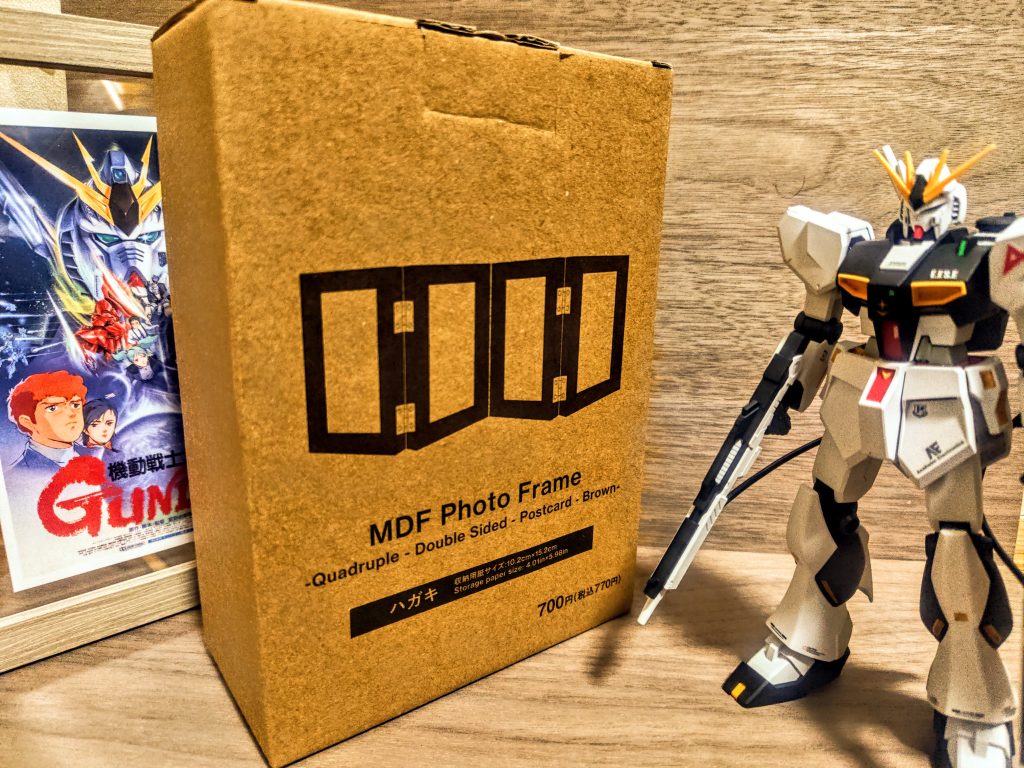 いつもはダイソーさんの写真立て(ポストカード立て)に何かしらのポスターを入れてその前にキットを置いて飾るんですが、今回凄くいいのを見つけたので思わず紹介。この更新はガンスタ様の趣旨から少しずれそうですが、せっかく皆さんが作ったガンプラを楽しくし飾るために、という思いでアップします。購入したのは、ダイソーさんの姉妹店、スタンダードプロダクツさんから発売されている立体フォトフレーム。もちろんポストカードサイズのものを購入しました。これがまたなかなか悪くないアイテムなんですよ。