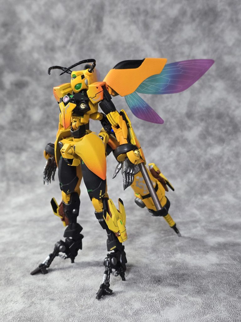 型式番号：GN-008QB　機体名： GN QUEEN BEE　【GNクィンビー】GNアーチャーをベースに、人革連の「超兵計画」によって生み出された実験体の一人が搭乗することを前提に大規模改修された特殊急襲型MS。蜂を想起させるそのシルエットは、GNアーチャーの基礎となった「ガンダムアルテミ―」を彷彿とさせ、高機動戦闘能力と、戦場全体を支配する高度な情報収集能力を両立している。最大の特徴は、尾部に搭載された「ツインドライヴ・ユニット」である。2基の太陽炉を直列に繋ぐことで、瞬間的な粒子出力を極限まで高めているが、その代償として機体バランスの維持と粒子制御は困難を極める。これを制御するため、機体頭部に有機的な形状へと進化したクラビカルアンテナを配置。戦場の微細な粒子変化を読み取り、パイロットの脳量子波とリンクすることで、人外の反応速度を実現している。