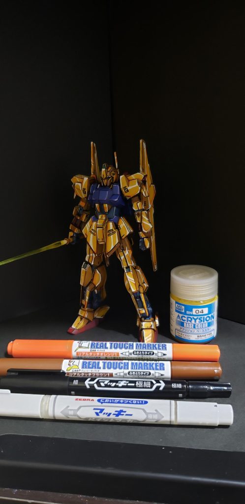 今回は金色部分はベースイエローを筆塗りしたあとはペン類だけでいけました。影色はリアルタッチマーカーのブラウンの太い方のペンの腹部分でなぜるようにするだけです。とちゅうでオレンジのが良かったと思い追加で影色を増やしました。ハイライトはマッキーのホワイトの細い方のペン先で。エッジ線もいつもの普通のマッキー黒です。肩の百もマッキー黒の細い方で書いてます。