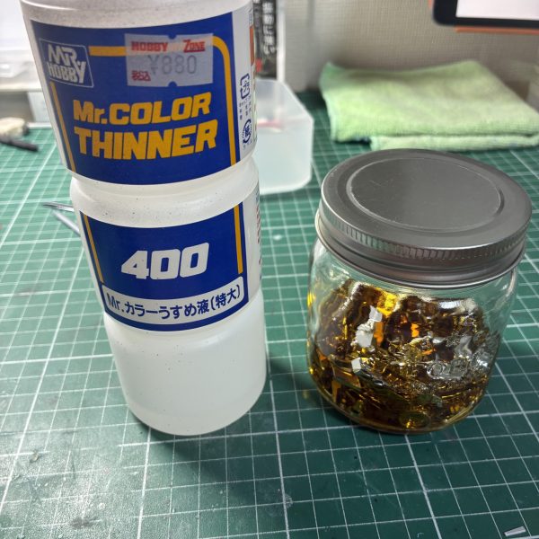 はじめてのメッキ剥がし【用意したもの】・クレオスうすめ液・蓋つき瓶 100円×2・ドリッパーのフィルター・キッチンハイター(塩素系)調べても工程を些細に記載したものがなかなか見つからないのでまとめました以下、工程【写真2〜4枚目】・ゴールド部分を剥がす作業・メッキではなくクリアイエローを剥がす作業なので、ランナーから落としたパーツを瓶に入れてシンナー風呂・漬けた瞬間から液剤は黄土色に染まるぐらいにはスピーディーに色が抜けていく・蓋つき瓶にした事で寝かして振ったりが可能だったのでムラなく色を落とすことが出来た・5分もかからずゴールドは無くなる・濾過作業は5回ほどに分けて少しずつ。紙フィルターは片付けも含めて慎重になる必要がなく正解でした【写真5〜7枚目】・本題のメッキ剥がし・ハイターにも色々と○○系というような種類があるようで、実例で見かけるキッチンハイター(塩素系)を用意した・長物は平らなトレーに…しましたがゴールドと同じく瓶に突っ込んで振った方が早かった・漬けて2分ほどで小さいパーツはメッキが溶けて下地の乳白色に・瓶を寝かして転がしたりでこちらも5分とかからず全てのパーツが下地の乳白色に・失敗したなと思ったのはハイターは泡立つので振りすぎ注意。泡で取り出しにくくなる上に今回のように乳白色のパーツは取り忘れがないか見分けにくい。正しく「漬ける」でいいと思った 【やってみての感想】・想像以上に時間がかからない。洗う時間のほうが長い・突貫なら総作業を30分ぐらいでやれそう・メッキごとに特長もあるようなので、今回はガンプラメッキの場合の結果でおさめようと思う【良かった点】・濾過用にフィルターともう一つ瓶を用意したこと・蓋つきの瓶【反省点、困った点】・ハイターを泡立たせた・プラモだけの用事にしてはハイターのボトルがデカい・洗い物が多い以上です。何かの参考になれば(2枚目)