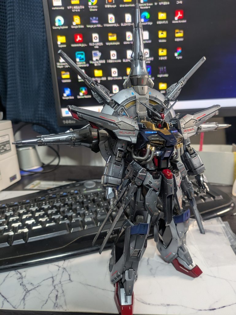 部屋のLEDシーリングライトのみの光源だとこんな感じで濃い銀色に。パール塗装の妙ですね。ところで、机の上で撮るガンプラっていいですよね。なんだか今にも動き出しそうな感じが好きです。