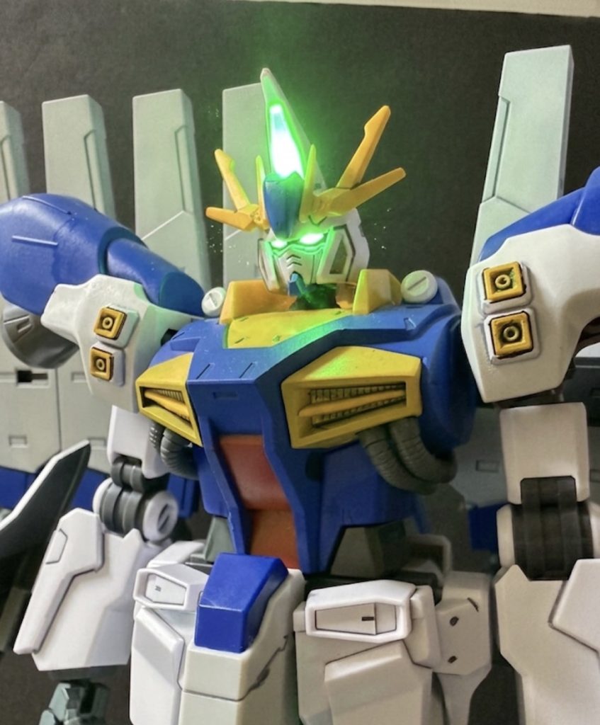 ※写真はサイコフラッシュの発光準備に入るペルセウスガンダム■サイコフラッシュ①（Psycho Flash）サイコフラッシュは、ペルセウスガンダムに搭載された対サイコミュ兵装無力化システムである。機体頭部に内蔵された発光装置から特殊な高密度光信号を照射し、対象機のサイコミュ制御回路へ干渉することでサイコミュ兵装および関連機能を一時的に無効化する。照射時間は最大5秒と極めて短時間であるが、光信号は可視光と同時にミノフスキー粒子変調信号を含んでおり、照射範囲は基本的に「光が届く範囲」に及ぶ。対象機がこの光信号を視覚センサーやサイコミュ受信系を通して認識した瞬間、内部のサイコミュ制御プログラムに誤作動が発生し、サイコミュ・ブロックが強制的に停止状態へ移行する。この効果はサイコミュ兵装やサイコフレームを搭載した機体に限定される。外装に露出したサイコフレームだけでなく、内部構造に組み込まれたサイコミュ・モジュールにも干渉するため、ファンネル、ビット、インコムなどの遠隔兵器の制御が遮断される。また機体に搭載されたサイコミュ制御装置そのものにも影響を及ぼすため、ニュータイプ用機体では一時的に反応速度や操縦補助機能が低下する。
