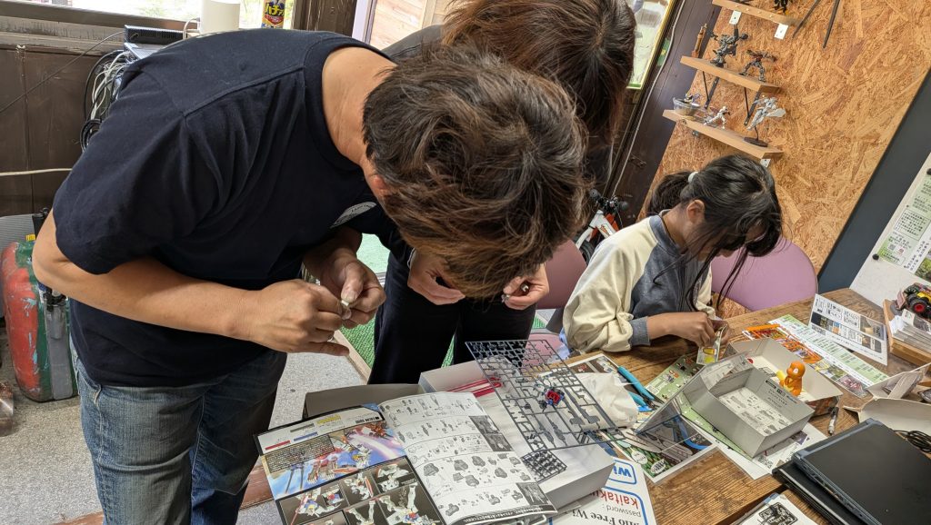 作品名：キャンプ場の受付で…<p>今回も当キャンプ場の受付のテーブルでご家族総出でガンプラにチャレンジしてはりました🤣 キャンプ場でガンプラ布教活動。楽しいですねー😻</p>
