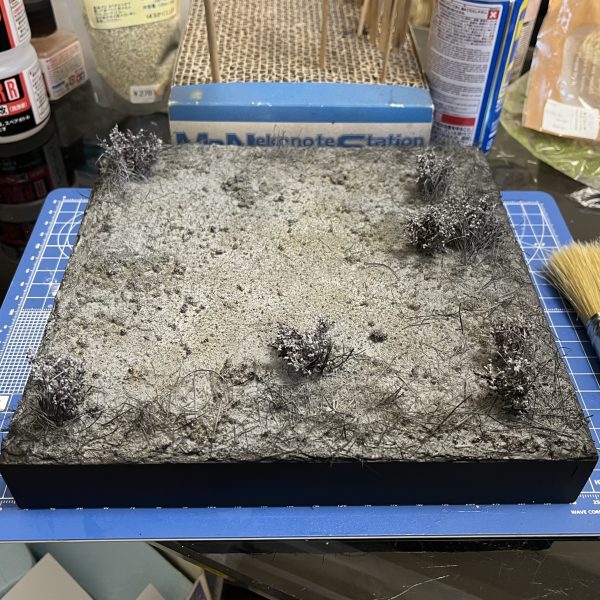 ジオラマの進捗状況です。黒の縁にマスキングしてベースの塗装を行なったら刷毛の毛をカットして地面に植え込み草を密集させます。地面表面にはスポンジの細かいかけらを振り掛けて背の低い小さな草を表現してます。（3枚目）