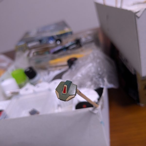 食玩アーティファクトのスタークジェガン。まずはスカート周りのパーツから、筆でちまちまと塗り進めています。​この小ささですが、UCのシブい世界観を出したくて、色のトーンを落としつつ細かく塗り分けてみました。中央の赤が我ながらいいアクセントになってお気に入りです。が、なんだか渋すぎるなーと一日悩んだ結果、塗り直し。せっかく作るので、こだわってみたいなーということですかね。&nbsp;メインの写真にしている連邦マークは、奇跡的に塗り分けができました。中途半端だったので別パーツにしてみたのですが、削りカスと見分けがつかないくらいなサイズになってしまい、不安だったのですが、思いのほか上手くいってよかったです。​まだまだ先は長いですが、じっくり形にしていきます！（3枚目）