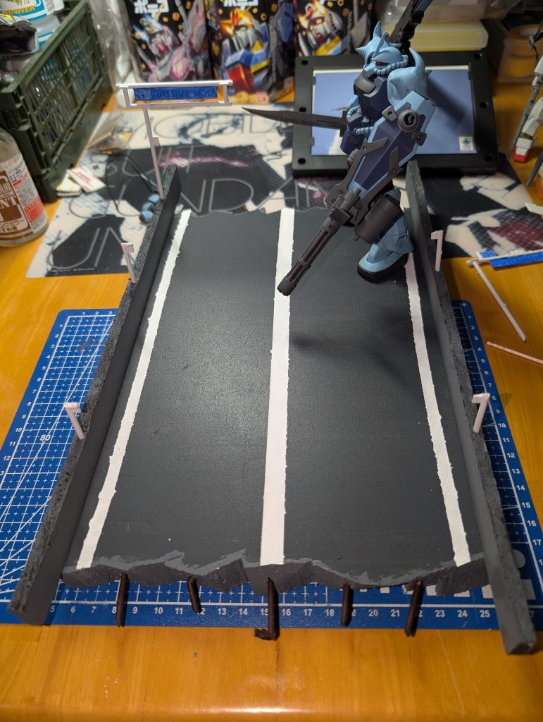 一度、情景セットみたいな物を自分で作れたら良いなぁと思っていたので、そっちをチャレンジする事にして皆さんガンタンクを土台にして名シーンを再現されていて憧れていたんですが😳ガンタンクを作った事がなく、キットを犠牲にする度胸も無いため😱、100均のやつなら心も痛むまいと頑張ってみました100均のポリスチレンボードの端っこをザク切りし、100均のアクリル絵の具で塗りたくり、マスキングテープを絵の具で白く塗り、折れた鉄筋・街灯・道路標識はランナー片を切って突き刺しました。標識は何も考えずに青で塗ってしまい、「高速道路じゃなく一般道やんけ😨」となってしまいました💦