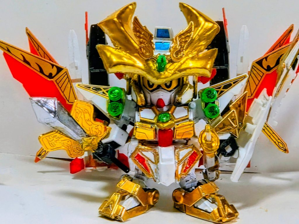LEGEND BB 武者頑駄無をベースに他の方の作例を参考に元キットの鎧を武者頑駄無の鎧パーツに切り貼り、足の装飾と腰鎧の一部、腕、鳳凰結晶に二代目頑駄無大将軍のパーツを使用、元祖SDの隠密将軍(頑駄無副将軍)の腕パーツの内部の接続ピンをカットして新たに接続用のプラ板を取り付けて腕鎧にしています。兜は元キットのままだとパッケージや漫画版とイメージが異なるので頬にパテを盛ってヤスリがけを繰り返して理想の形に仕上げました。盾は隠密将軍の腕鎧の隠し針の先端を切断して接続しています。鳳凰の頭部も同様の方法で接続出来ますが少し斜めにしないと取り付けられないのと盾ほど安定せず撮影時にポロっと落ちるので今回は盾に取り付けました。