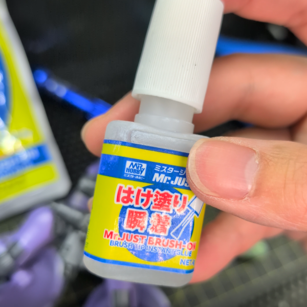 一番緊張する「異規格キット同士の接続軸改造(ミキシング)」に着手しました。今回は、リック・ドム(GQ)の腰部とゾックの上半身を接続するため、双方の元の接続ピンを思い切って切り落とし、新たにピンバイスで1mmの穴を開けて真鍮線を芯として通しています。この工程において一番苦労したのは、「とにかく穴位置をズレずに貫通させること」でした。相手は巨大なゾックのパーツ。1mmという極細の線とはいえ、コンマ数ミリでもピンバイスの角度が狂えば、パーツ同士に不自然な隙間ができてしまうため、文字通り息を止めるような思いで慎重に穴を開けました。結果的にズレることもなく、無事に真鍮線を通すことに成功!固定にはGSIクレオスの「Mr.ジャスト(はけ塗り瞬着)」を使用しています。このような繊細な軸打ち箇所において、はけ塗りタイプは液が余分なところに垂れたり白化したりする心配がなく、真鍮線の周囲の隙間だけにピンポイントで流し込めるため非常に重宝しました。真鍮線を芯にして強固に接着したため、強度も申し分なくガッチリと留められており、この仕上がりには大満足しています!(2枚目)