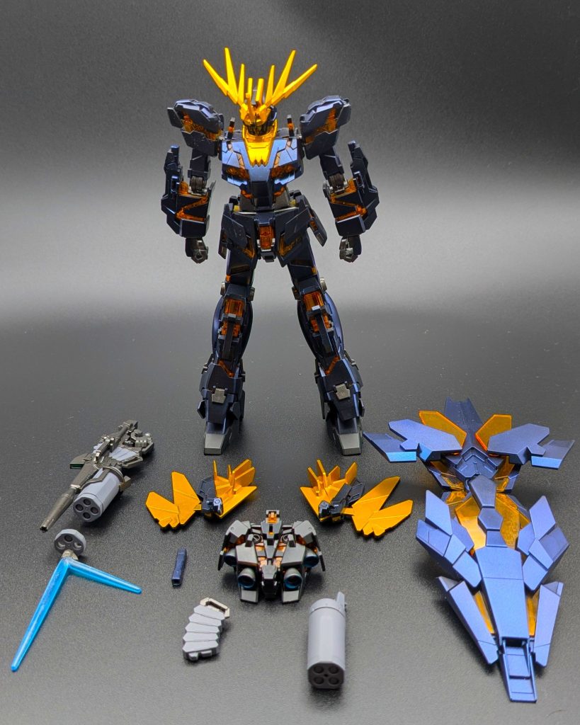 付属品一式を並べたカットです。リボルビング・ランチャー、ビームマグナム、予備の角パーツ、頭部、バインダーなど、フル装備の内容が一目で分かります。
