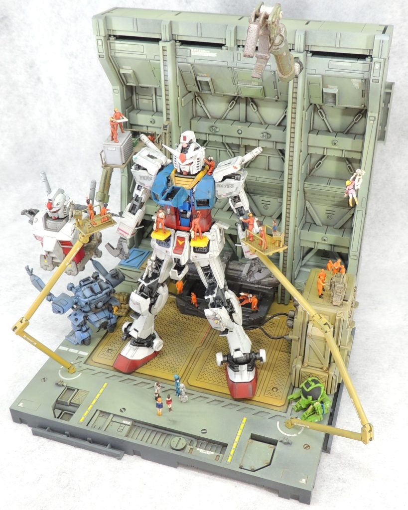 向かって左下にある白と赤のガンダムの上半身は、旧キット1/144プロトタイプガンダムのパッケージに対するオマージュです。ドラケンはジム・スナイパーⅡのキットに付属しているものを流用しました。ガンダム背面の黒い巨大な装置は、MG1/100ガンダムエクシアの太陽炉のディスプレイベースにスターウォーズ関係のパーツを取り付けて自作しました。