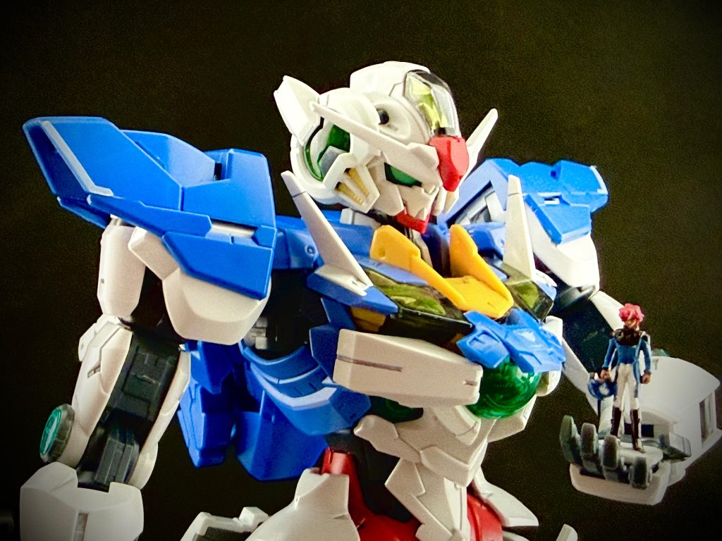 グラハム•エーカー（以後“グ“）「久しぶりだな。少年」刹那•F•セイエイ（以後“せ“）「…お前は」グ「…なに、新しいガンダムがある。と聞いてな」せ「……」グ「…ほう、これか、…遠目には、“エクシア“。少年のガンダムに見えたが。…これは、…エアリアル」せ「…ああ、そうだ。コビト少佐が、1/100フルメカニクスガンダムエアリアルに、MGエクシア、ダブルオー、クアンタなどの、主に外装のパーツを貼りあげて作った物だ」グ「ほう…」せ「…それに、未塗装だ」グ「…なんと。……つまり、これは、素組みと言っても差し支えないと…」せ「ああ、コビト少佐も“これなら塗装の剥げを気にせずブンドドできる“と言っていた」グ「…フルメカニクスのエアリアルは良く動くからな。良い選択だ。正しく、“愛“だな」せ「ああ、同意する。…だが、問題もあった」グ「ほう、それは？」せ「今回の投稿の為に、撮影をしていた時に、左肩、胴体側の引き出し関節の部分がプラっプラになった。原因はわからないが、コビト少佐は、“軸の受け側が割れたのかも“とは言っていた。…“これじゃ、格好良いポーズが取らせられ無い！“と言って、悶絶していた」グ「…で、その後、どう対処を」せ「…涙目になりながら接着していた。…まあ“可動はしんだが、肩幅が少し広くなって男らしくなった“と、自分で自分を慰めていたが…」グ「臨機応変に対処する、…心眼は鍛えているようだな。…だが、そう見ていくと、エアリアルは比較的最近のキットだ、それに対し、MGエクシアを始めとする一連のキットは、素材にABS樹脂を多用している上。よもや十年以上も前の物になる。…やはり、いろいろと大変だったのではないか」せ「…ああ、そうだ。コビト少佐が昔飾っていたこれらのキットを出した時、ABS樹脂を使用している部分、関節などは大体クタクタになっていた。…エクシアは特に」グ「…辛いな、少年」せ「いや、大丈夫だ。…エスカッシャンのギミックを思いついた時に、最も大変だったのが、クアンタのGNシールドのバインダーを保持するアーム部分だ。ユルユルになったアームでは、エスカッシャンのパーツをつける為、重くなるバインダーを保持出来なかった」グ「…確かに。それでは、シールドを跳ね上げたり。と言った格好良いポーズを取らせられないな。……触っても？」せ「…ああ、かまわない」グ「……フフ。…抱きしめたいな。ガンダム」せ「…やめてくれ」グ「…すまない、冗談だ。……うむ、確かに、バインダーを保持するアームは何とかしなければな。…私はどの様な道理も、私の無理でこじ開けてきた。…どうにかしてみよう」せ「頼む…」グ「…男の誓いに訂正は無い。…良いか、少年。年の功と、という訳では無いが、方法がある」せ「…教えてくれ」グ「…フム、では、…こうして、爪楊枝の先に、瞬間接着剤をほんの少し、付けて。…こうして、軸部分に、こう、薄く塗り広げて。…こうして、…こうして、瞬間接着剤が乾かないうちに、キコキコしてやれば」せ「…………」グ「………。フッ。…動かなくなった。少年」せ「…ッ！貴様ッ！」グ「落ち着け。少年ッ」せ「よこせッ、俺がこの歪みを正す。…お前がやった歪みを、俺がこの世界を切り開くッ！」グ「…よせッ。少年ッ！…そこをそう持って、動かすと…」グググっ…。……モロッ。グ「…ッ！」せ「……ッ！！」コビト少佐「………ッッ！！！」せ「う、ウォォッ。…トランザムッ！」グ「…少年ッッ！！」〜後日。もげたアームの軸部分を、針金を入れ補強しながら、補修しているコビト少佐の姿があった。