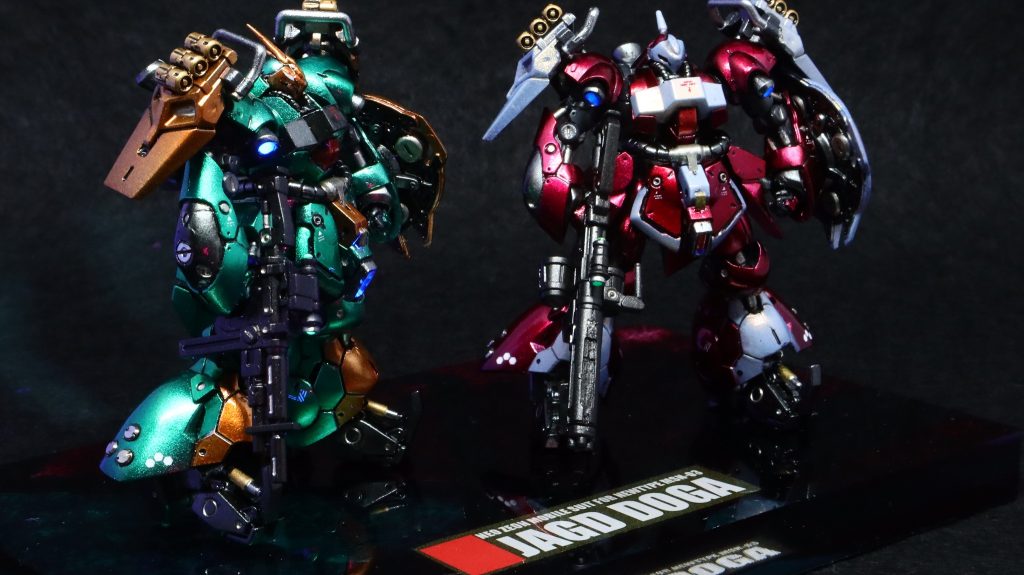 塗装はフレームをメカサフ+クレオスメタルブラック少々、装甲はグレーサフ→ガイア・アルティメットブラック→ガイア・スターブライトシルバーをベースに、クェス機の赤部はクレオス・クリアレッド、白部はガイア・クリアホワイト。ギュネイ機の緑部はクレオスのクリアグリーンとクリアブルーを8：2、オレンジ部はクレオスのクリアペールブラウンを使用。クリアホワイトは初めて使いましたが、マジョーラ塗装の様になって面白い表現です。元のキットの出来が素晴らしいので大きな改造は入れていません。甘いモールドの彫り直し、各スラスターの開口と成形、脚部モールドにハイキューパーツHSリベット2mmを設置しました。合わせ目消しは、腕はフレームのパーツ分割でできましたが、脚は私にはムリだったのでフレームを先に塗装まで済ませて外装組付けで瞬着で合わせ目消し→フレームを徹底的にマスキングで対応しました。一番苦労したのはモノアイです。クリアピンクHアイズ1mmをスライスして0.2mmくらいの薄切りにした上で成形し、目玉が飛び出ないようにフェイスパーツ側も彫り込んでから接着しました。老眼鏡大活躍。