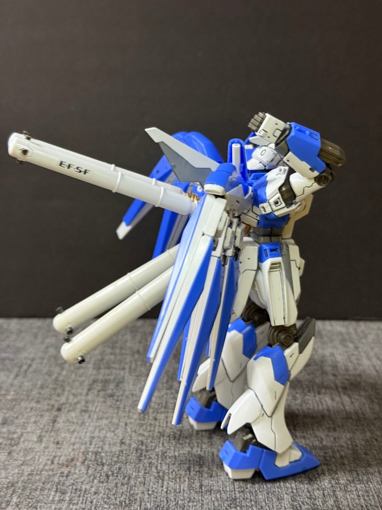 【機体解説②】最大の構造的特徴は、サイコフレームの配置と機体バランスの最適化にある。急造機ではコックピット周辺のみに配されていたサイコフレームを、本機は駆動系やフレーム主要部へ全面的に装填している。これにより、パイロットの脳波（感応波）による追従性は飛躍的に向上した。また、背面バックパックは「単一の大型スラスター兼兵装マウント」へと全面刷新され、左右に均等な質量配置を行うことで、機体の運動性・旋回性能における偏りを排除することに成功している。