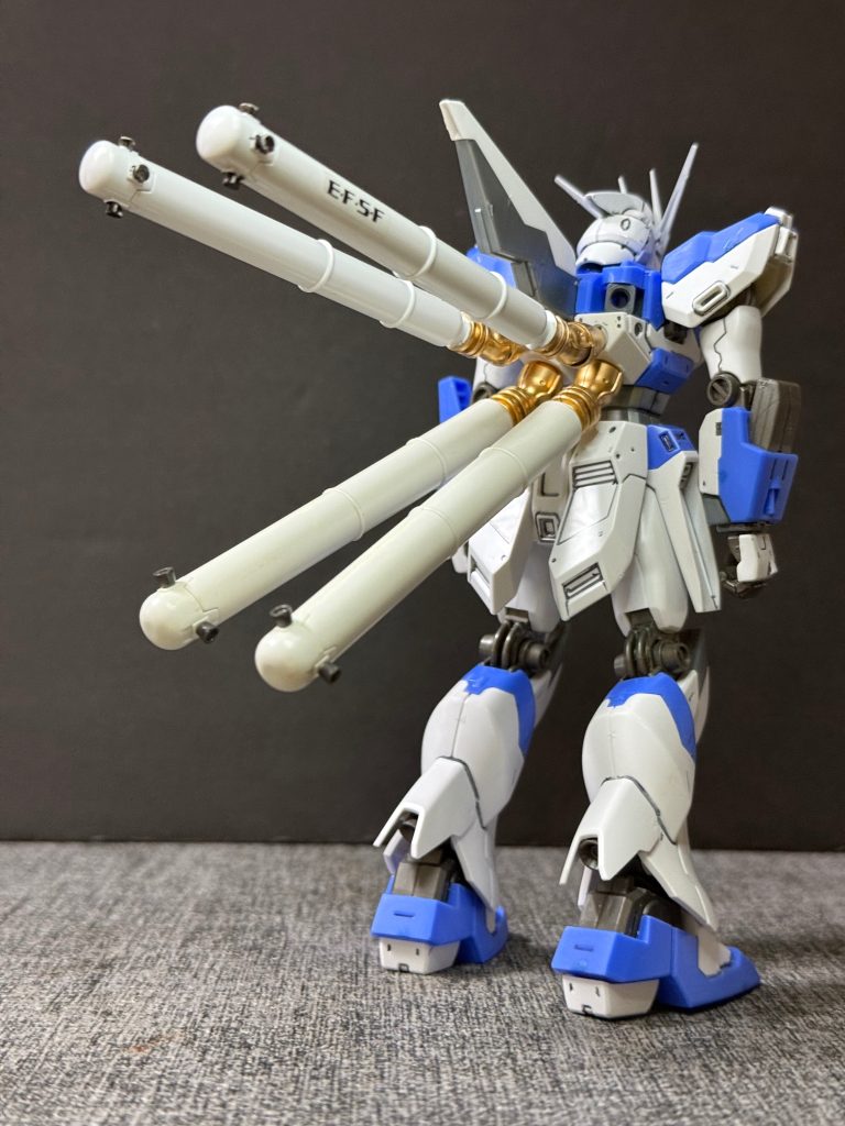 【改修計画】反乱軍によって最新鋭機「Sin-νガンダム」が鹵獲されたことで、地球連邦軍は従来のMS戦力では対抗が困難であると判断した。しかし、新型機を一から開発する時間的余裕はなく、既存のνガンダムおよびHi-νガンダムをベースとした緊急改修計画が立案された。本計画では、機体後部に大型プロペラントタンクをさらに2基増設し、推進剤搭載量を従来比約2倍まで増加。これにより、長時間の高出力機動および継続戦闘能力を大幅に向上させた。一方で、増加した質量に対応するためスラスターは常時高出力運転を強いられ、機体各部への負荷は極めて大きかった。&nbsp;本機は設計思想よりも実戦投入を優先した「応急決戦仕様」であり、機動性や運動性能を理論的に最適化した機体ではない。