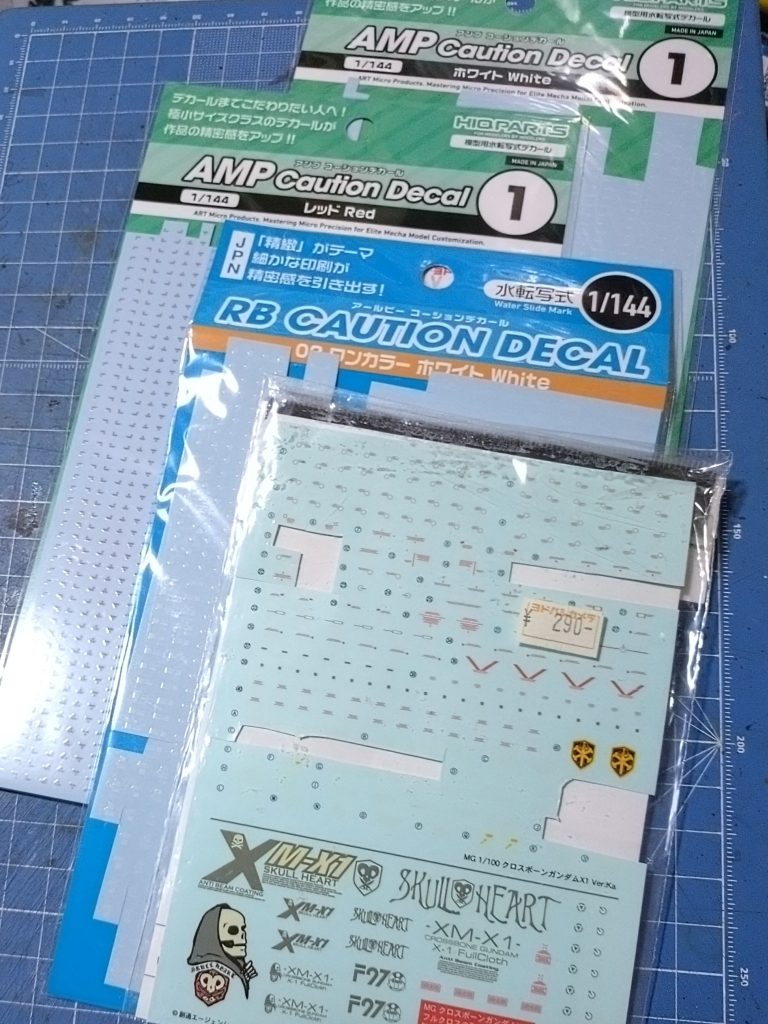 今回コーションデカールを貼って見たくて探した所、ハイキューパーツの１/１４４サイズを購入してきて使用、肩シールドと左足のミサイルポッドは面が広くて間延びする感じがしたので関係ないけれど古～いクロスボーンのマークを貼り付けてみました。