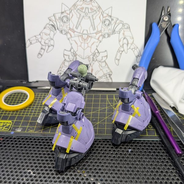 リックゾック(仮)の脚部パーツのスジ彫りに着手しています。今回はHG 1/144 リック・ドム ガイア機/オルテガ機(GQ)の優れた脚部パーツを流用しているのですが、最大の難関はリック・ゾック特有の「3本脚構造」です。以前、腕部の工作を行った際に、片方ずつ完全に作業を終わらせる直列方式をとったところ、後から「また同じラインを引かなければならない」という精神的な負担が非常に大きいことに気づきました。その反省を活かし、今回は同じ作業をいっぺんに終えられるように、3脚すべて並行して作業を進める手法に切り替えました。【こだわりの作業工程と使用ツール】まず、3パーツすべてに同時に「ニチバンクリアラインテープ」を貼り付けます。透明で下地が見えるため、左右対称(今回は3対称)のアタリをつけるのに非常に重宝します。次に「ケガキ針」で慎重にガイドをなぞり、「ラインスクライバーCS 0.15mm」を使って、1/144スケールに合わせたシャープな溝を彫り込みました。彫った際に出るプラスチックのめくれは「ミネシマキサゲ」で丁寧に処理してエッジを整えています。同じラインは同じタイミングで引いてしまうことで、対称性の精度が上がるだけでなく、何よりモチベーションを維持したまま作業を進められるので個人的にかなり楽になりました。複数の同じパーツを作る際、皆さんはどのようにモチベーションを管理していますか?ぜひコメントで皆さんの工夫やこだわりも教えてもらえると嬉しいです!引き続き完成に向けて楽しんで作っていきます。↓ラインテープ紹介(2枚目)