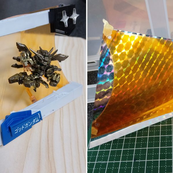 ①透明プラ板でカードベースを作成。背面はC字に曲げ、そこに側面を3ミリ軸で接続。UVレジンで複製して作ったちくわ状の３ミリ接続パーツをつけて隙間なく固定する形。やや斜めに傾いて採光できるようにしつつ、キャラを空間として包めるような形に。②ホロ部分はダイソーのホログラムデザインペーパーをテープで付けただけ。適当に何枚か買ってきたものだけど、最近仕様変更したのか輝き方が良いものと鈍いものがあるので、より輝いてる方を使用。額縁となるカードフレーム部分は同じく100均の連結ディスプレイベースの端を切り取ったもの。ネームプレートと太陽マークの土台部分は３０ｍｍのティルトローターのパーツ。ゴッドガンダムの名前部分はＲＧシャイニングに付属のランナーから。カードフレームは当時もちょっとダサさを感じてたので、ついでに立体物として奥行きを見せられるような形に少しだけアレンジ。③透明プラ板はクリアオレンジで塗装。回転させて横の側壁が見えてもなるべくキラキラ空間が繋がって見えるように。側壁の外側に直接オレンジホロペーパーを貼るよりかはこちらの方が自然に見えたので。④カードフレームの太陽マーク部分は、100均の☆マークの型からUVレジンで作成。中には銀のホロペーパーを下地に透明ホロペーパーも少し入れた。☆部分の真ん中だけ丸くへこんだ造形になってるので、ホロの輝きだけでなく物理的な屈曲によっても表情が出せるように（写真だとほぼわからないが）。中心の☆は３ミリ軸接続、他の小さな部分はUVレジンの硬化で接着。硬化後のポロリが恐いのでUVレジンでの接着は少しはみ出すくらい塗ったが、見映えなど良くなるようにここはもっといい方法を考えていきたいところ。他の文字や数字も100均のレジンの型から作った。　背面の集中線のような演出パーツも作成。ダイソーのラッピングタイにUVレジンを薄く塗って輝かせつつ形を固定、数本を中心で束ねてネオジム磁石も添えてレジンで接着。このラッピングタイは空間に線のようなラインを入れるのに重宝しそう。　カードベース側にはマグネットシートをテープでくっ付けるだけ。後ろは見えないので適当。カードベースは底面と後ろも横にランナーを通して３ミリ穴パーツでさらに固定、中央と側壁の隙間をなくしていく。⑤物理的なキラホロエフェクトも製作。クリアオレンジで塗った透明プラ板に透明ホロシールを貼ってUVレジンを塗る。やや水っぽい質感になってしまうが、ちゃんと光を反射して存在感を持って欲しかったのでレジンは厚めに塗った。⑥右の側壁は縦に長いものも用意して、パース付きカードダスにもなるように。これでカードベース部分の工作はおしまい。（3枚目）