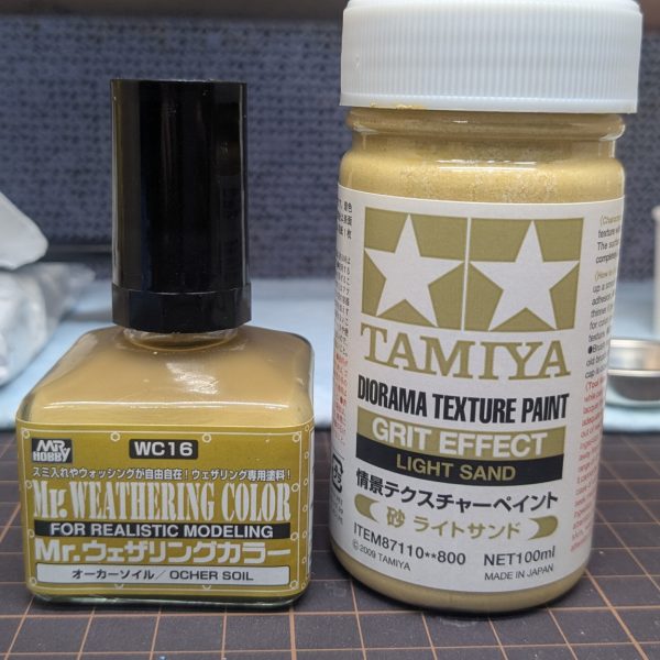 水溶き紙ねんどの隙間からブルーが見えてしまってるので、ダイソーのジェッソで隙間埋め。その後は鉄壁の組み合わせ、タミヤのテクスチャーペイントとウェザリングカラーのオーカーソイル。凹んだところや影になるところにオーカーソイルを置くと、ジワッと広がってくれて砂漠に自然な表情が出ます😊（2枚目）