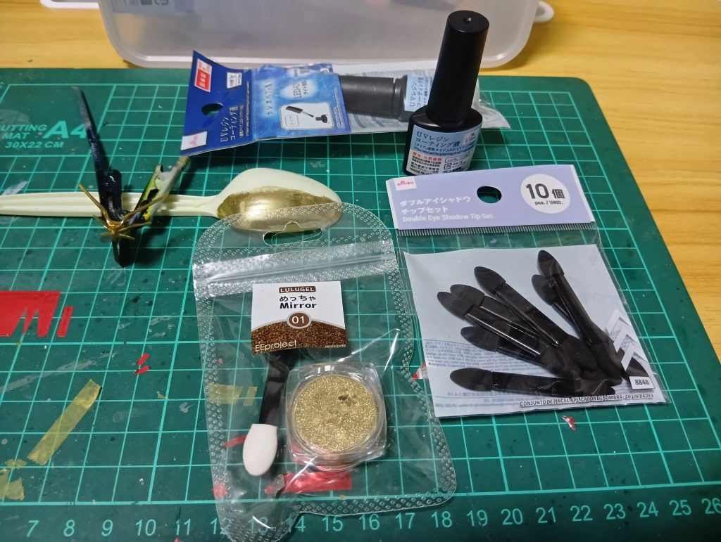 「めっちゃミラー」で検索したら出てくるやつ。本来はネイルをメッキ風にするヤツ。「トップコートにこすりつけるとメッキ風に」という触れ込みなんで試してみました。下地なんですが、スプーンでもお分かりの通り明るい色はムラが目立つようです。黒か金で安定するようです。そこにトップコート塗ります。我々御用達のクレオス艶トップコート缶スプレーでは定着量が弱かったです。厚塗りすればどうにかなるかもしれません。また通常のネイル用のトップコート（艶あり速乾）も表面が硬すぎるのかダメでした。で、画像の上の方に移ってるダイソー産のUVトップコート。最近はネイルコーナーに置いてなくってアクセサリー作りコーナー専門みたいです。これを塗ってUVライトしたあと、ミラーパウダーをアイシャドウ用のチップ（黒い棒のやつ）でこすりつけていきます。先端に少量つけてグイグイ押し付ける感じ。柔らかい下地に細かい金属片をぶっ刺していくイメージです。なのでトップコートにある程度の柔らかさと厚みが求められるようです。ピカピカに♪で、恐らくパウダーには全く接着要素がないので時間経過で深刻な「粉落ち」が起きるはず。接着されているはずのメタリック系の塗料ですら金属粒子の粉落ちが起きて経年劣化するんだからね。だからこの上からのトップコートが必要。ですがそこは答えに心当たりあり。メッキ風の上からトップコートするとほぼほぼ曇って、鏡がステンレスぐらいまで落ちちゃうんだけど、タムタムとかで売ってる車やバイクに使えるガラスコーティング剤でOKのはず。3000円ぐらいしちゃうんだけどね(gundam-kao9)OKでした♪