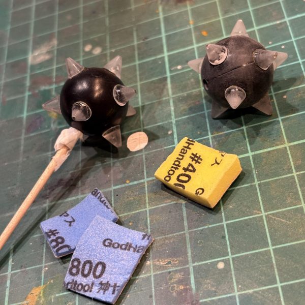 こちらのページまでご覧くださり、ありがとうございます。こちらはターンエーハンマーの製作記録です。本体記事にも書いた通り、RG武器セットがあれば何の苦労もなかったのですが…。特に2個が難関💧ということで球体部分を探す旅に。YouTubeでコジマ大隊長さんが「100均の軽量スプーンの柄を切って貼り合わせると、球体ができて便利なんですよ」と話していたので買いにいったものの、5本セット＋適したサイズはその中の1つだけ。スプーンは半休なので玉2つ分には×4袋…。さすがに16本余る他の軽量スプーンの使い道がないので断念💧とダイソーをさまよっていると、おもちゃコーナーになんか手頃な玉！しかも2つ！ということで素体は指で遊べるミニボウリングの玉を採用です。チェーンは友人に買ってもらった赤いガンダムのハンマーより1本。もう1本は数日メルカリで地蔵（←売り場でやったらダメなやつ）をしてると、手頃な価格で同じく赤いガンダムハンマーを出品して下さった方が現れ、無事解決。ただ、あのハンマーはさすがに形状が令和すぎるので…最後はとげ。今回ご協力いただいたのはFGシャアザク。の肩。ここをレジンで型取りし、大量のアポロチョコミニを生産します。サイズが小さく気泡や割れができやすいので、選別→ヤスリがけの地獄作業。最後はそろった材料の組み合わせ…ですが、球体のどの位置にいくつトゲ！？のバランスが意外と難しく、ネットで色々な画像を調べてインデックスであたりを付けて調整…最後はフィニッシャーズのパテで傷埋め、サフを吹いたら完成！…まだ粗が目立つ？黒に塗っちゃえば分かりません（笑）というわけで最後はガンメタで塗装。鎖は可動して塗装がはげそうなのでメカサフヘヴィをうっすら乗せる程度にしました。苦節数ヶ月…何とか思い描いてたハンマーをターンエーに届けることができ、満足しています！笑&nbsp;（5枚目）