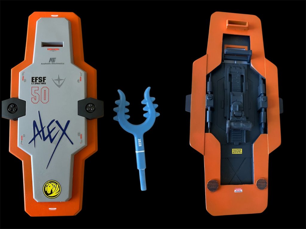ガーディアンシールドというらしいです。持ち手はガンダムかジムのシールド余剰パーツを付けて低い位置でも持てるようにしています。シールド裏はスカスカだったのでプラ板で埋めました。真ん中の武器は、ちいかわに出てくるハチワレの武器？の刺股（さすまた）です。チョコレートのふろくとして付いてたので持ち手部分を少し加工して持てるようにしてみました。