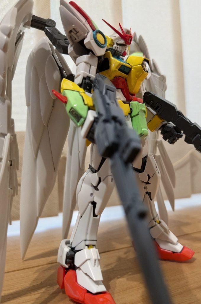 逆サイドからあおりで1枚。色レシピは次の通りです。白:成形色黄色:イエロー(顔サイド、肩ポイント、胴体、腕周り、スカート周り)水色:浅葱色(胸カバー、肩ポイント)オレンジ:オレンジ(胴周り、腰ポイント、腕の羽、スリッパ部分)赤:ガンダムレッド(マーカー。アンテナ、肩ライン)緑:ガンダム蛍光グリーン(マーカー。肩、腕装甲、スカート周り)金:ガンダムゴールド(マーカー。ゼロシステム) カメラ関係はあえて透明のままと、カメラアイはシールをそのまま採用。 てか最初のとことかタイトルで「ウイングゼロEW」って書いていて、どうにも自分的にしっくりこない…。俺ら世代はたぶん「ゼロカスタム」なんですよね(笑)