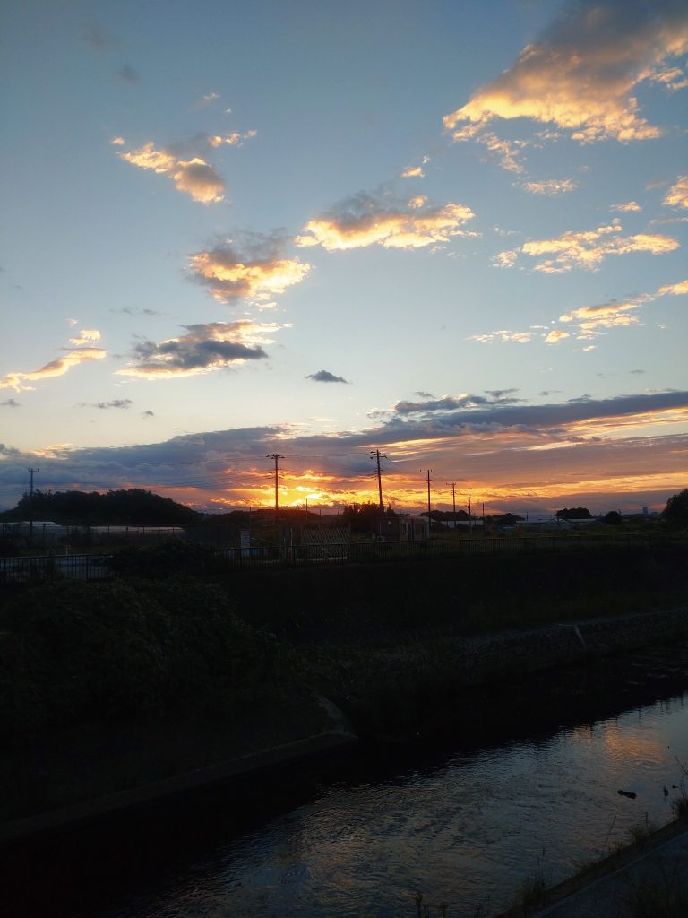2026年10月22日の朝6時の家の近所です。ウルトラマンは夕焼けですがその時間は人通りが多いので朝焼けを狙って撮影しました。皆さん健康的ですね。朝のお散歩のおばあちゃん、ジョギングするミドルエイジ、犬の散歩しているお姉さん。行き交う人の中で50過ぎたオジサンが1人、スマホとガンプラを空に掲げて撮影してる…。