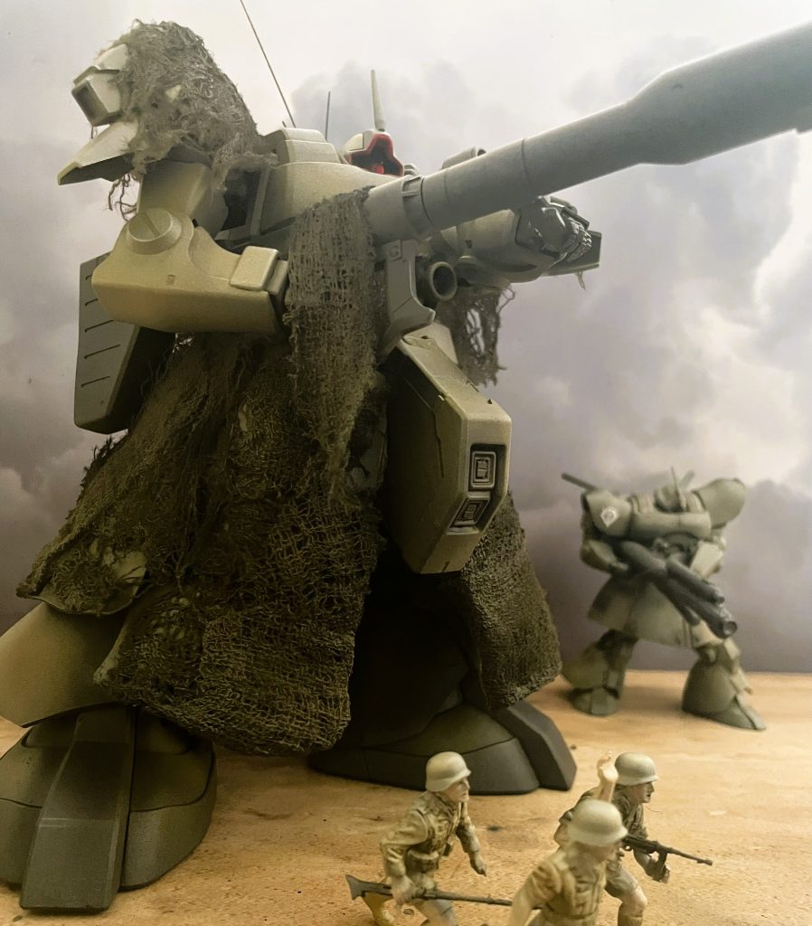 手前にタミヤ1/35ミリタリーフィギュアを3体配置して臨場感を演出しました。スケール差を使った空間演出を意図して1/220地上戦用ドムを後方に配置しています。