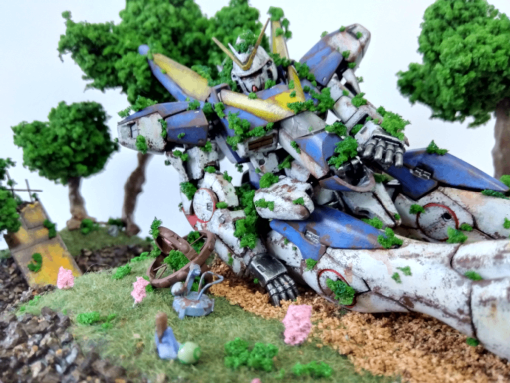 V2は筆塗りとウェザリングをして仕上げています。周辺には付属のシャクティのフィギュアの型をとって作成した少女とハロ、ヤナギランの花、エンジェル・ハイロゥのキールーム、持ち主不明のワッパを置きました。写真の左奥にはエンジェル・ハイロゥの外壁の残骸もあります。作品を見た人が色々なストーリを想像できるようなアイテムを置きました。Vガンの劇中未使用曲に「生まれてくるものへ」というものがありそれをイメージしながら構成を決めていったので、その曲を聴きながら楽しんでいただけると嬉しいです。