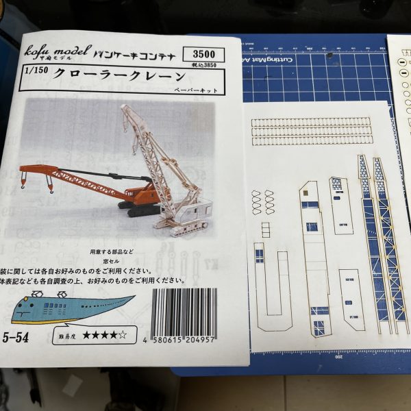 完成間際で唐突にクレーン車が追加となりました😅。昨日、名古屋大須のキッズランドへお目当ての瞬間接着剤とフィギュアを探しに行ったのですが見つからず…鉄道模型コーナーを物色しておりましたらペーパークラフトのイイ感じのクレーン車に目が釘付けとなりました。劇中でもコンテナの手前にそれらしき物が写っておりましたが、なんとまあ、この場にふさわしい小物か！見ての通りの紙とは思えない出来高です。という事で即座に購入。ガンプラよりも高価です…😅接着済みの廃材パレットの位置を変更しクレーン車の設置スペースを確保する必要があります。紙ですが塗装は普通にできるそうなので色もこれから決める予定です。今回のジオラマ、小物にかなり費やしましたがそれに見合った、まさにタイトル通りの出来栄えになると思います。（4枚目）